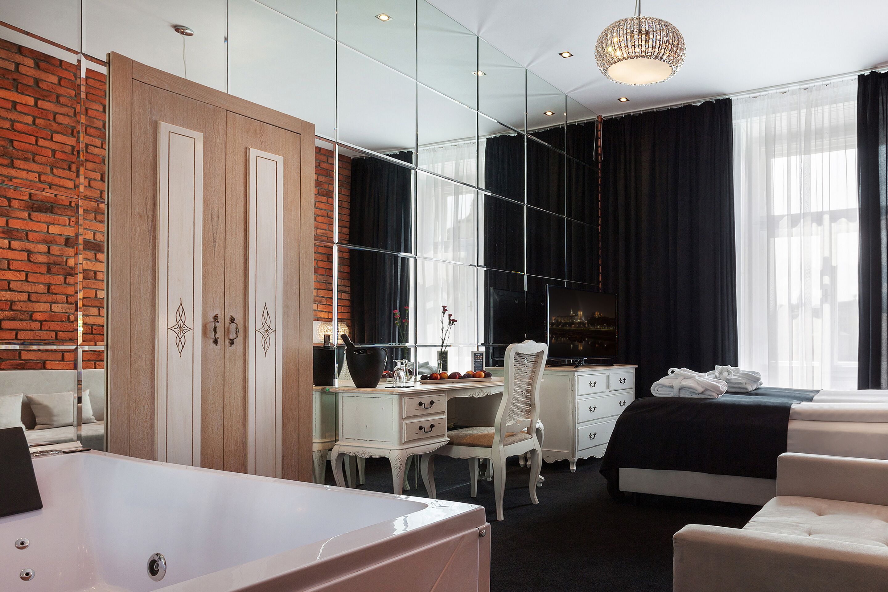A modern hotel room with a large mirror, a desk, a chair, a bed, and a bathtub.