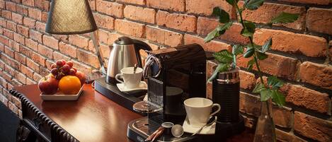 A wooden table with a coffee maker, cups, a vase with a rose, and a fruit bowl.