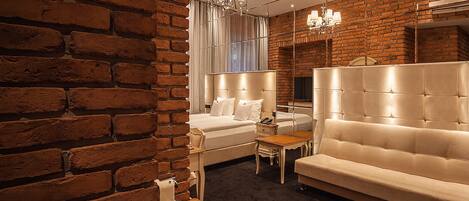 Una habitación de hotel con pared de ladrillo, una cama, un sofá, una mesita y un espejo.