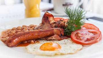Un plato de comida para el desayuno con salchichas, tocino, frijoles, un huevo frito y una rodaja de tomate.