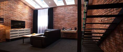 A modern living room with a brick wall, a sofa, a coffee table, a TV, and a staircase.