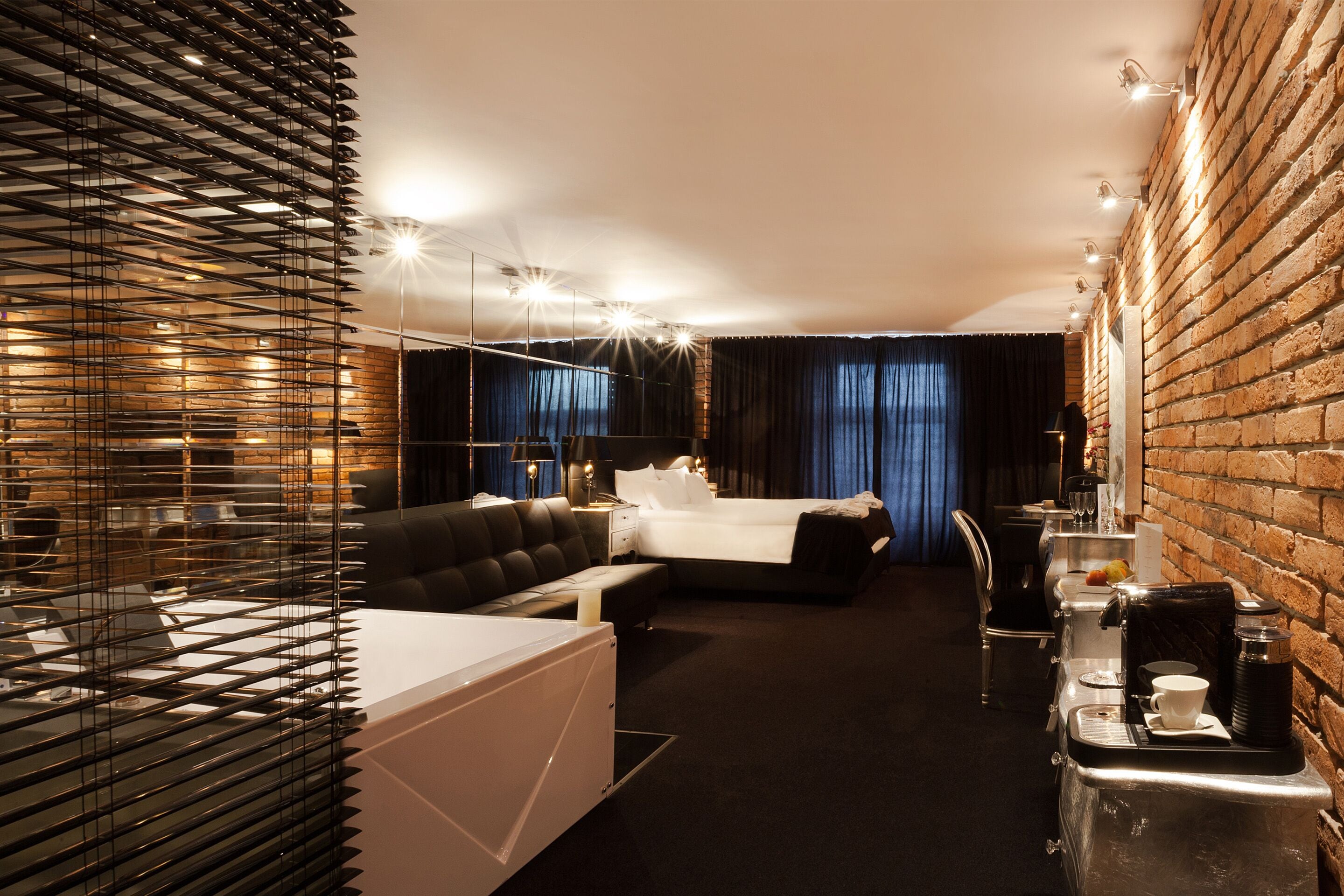 A modern hotel room with a large bed, a seating area, and a dining table with a coffee machine.