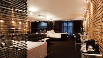 A modern hotel room with a large bed, a seating area, and a dining table with a coffee machine.