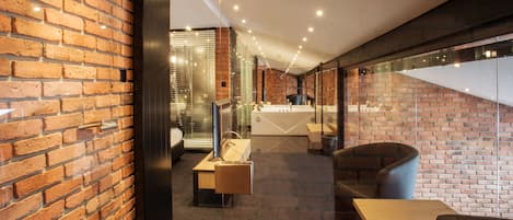 A modern interior with brick walls, a glass partition, a reception desk, and seating areas.