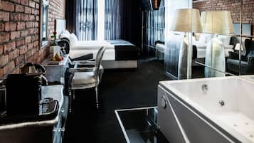 A modern hotel room with a brick wall, a large window with curtains, a bed, a desk with a chair, a bathtub, and a lamp.