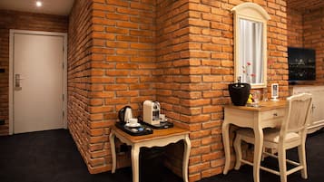 Une pièce avec un mur en briques, une porte blanche, une petite table avec une machine à café, une chaise et un téléviseur fixé au mur.