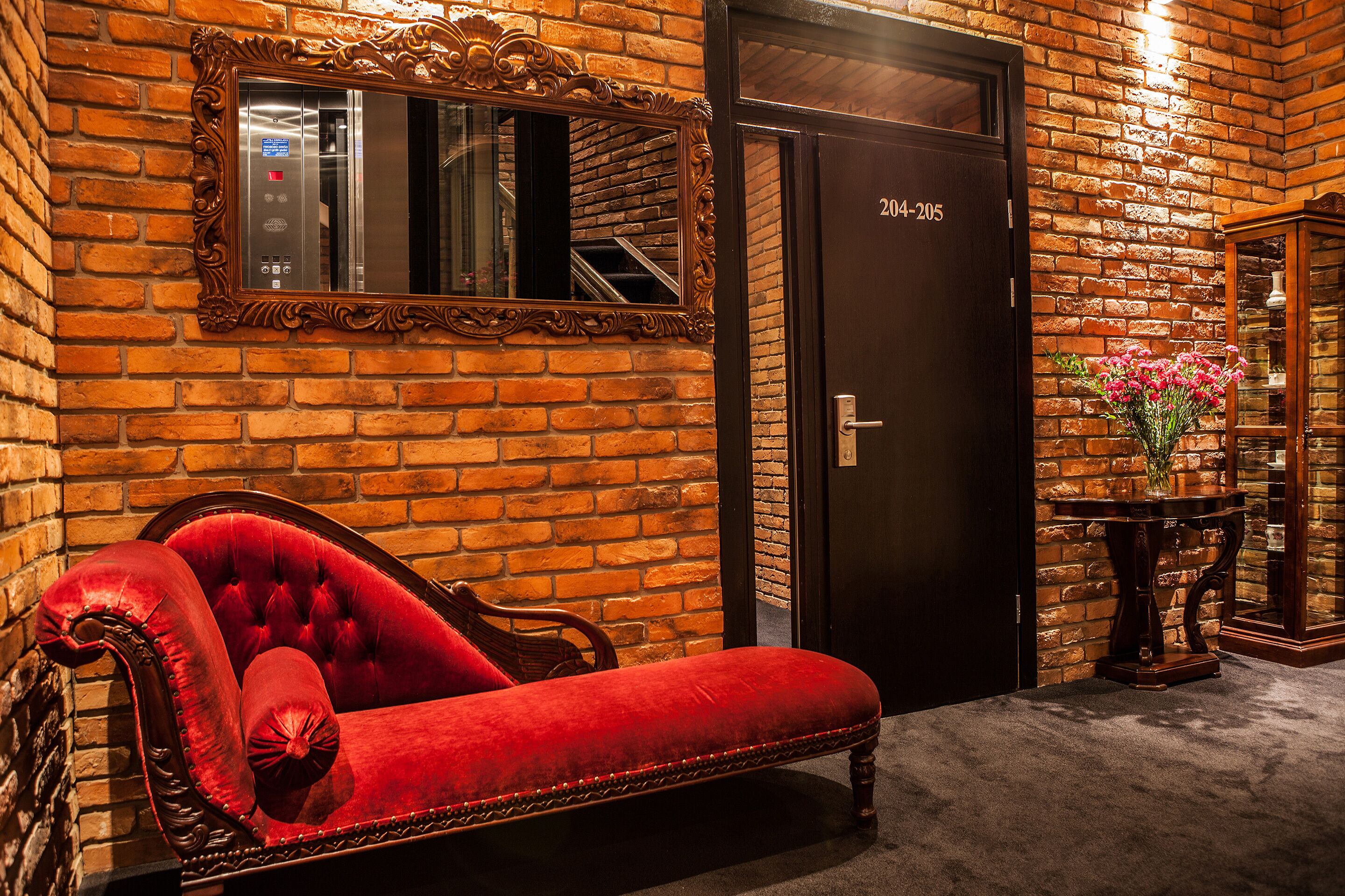A red velvet sofa, a mirror, a door with a number, and a small table with flowers.