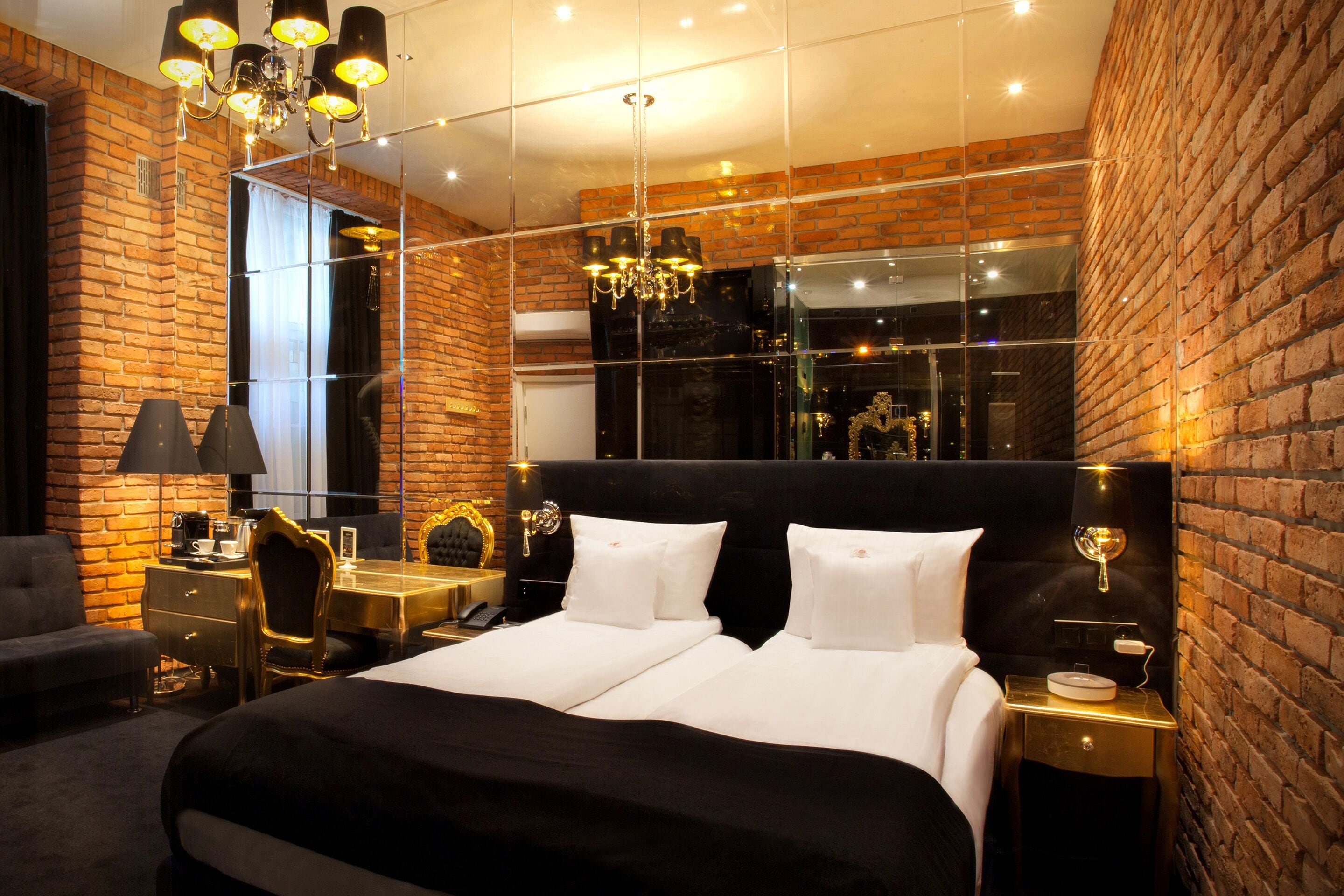 A modern hotel room with a brick wall, a large bed, a desk, and a chandelier.