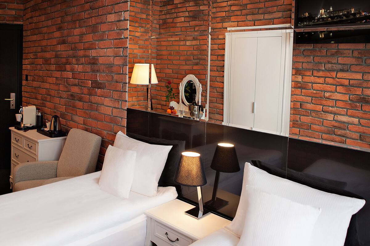 Ein Hotelzimmer mit Backsteinwand, einem Bett mit weißer Bettwäsche, einem Nachttisch mit Lampe und einem Spiegel.