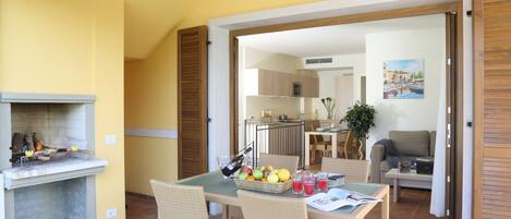 A dining area with wicker chairs, a table with a basket of fruit, and a fireplace.