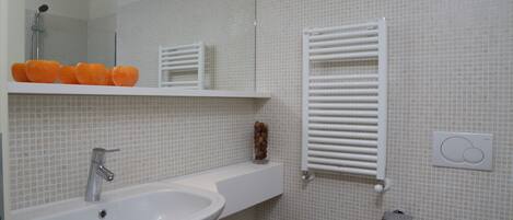A modern bathroom with a large sink, mirror, and a towel rack.