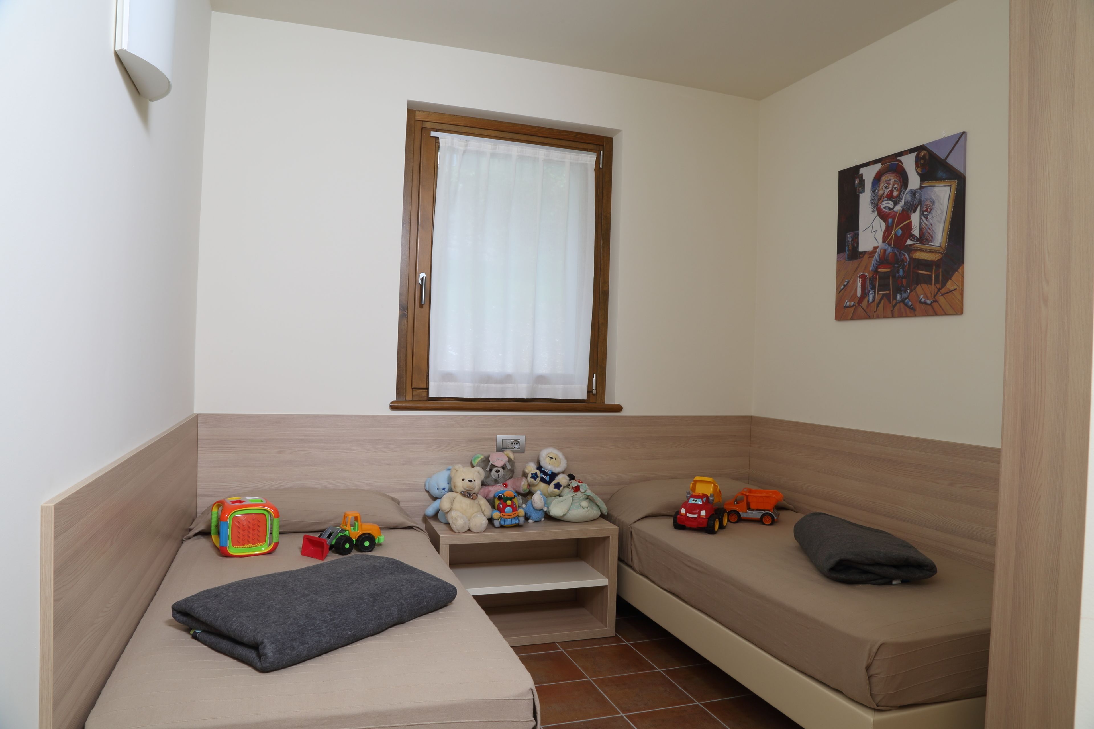 A small room with a bed, a sofa, a window with a curtain, and a painting on the wall.