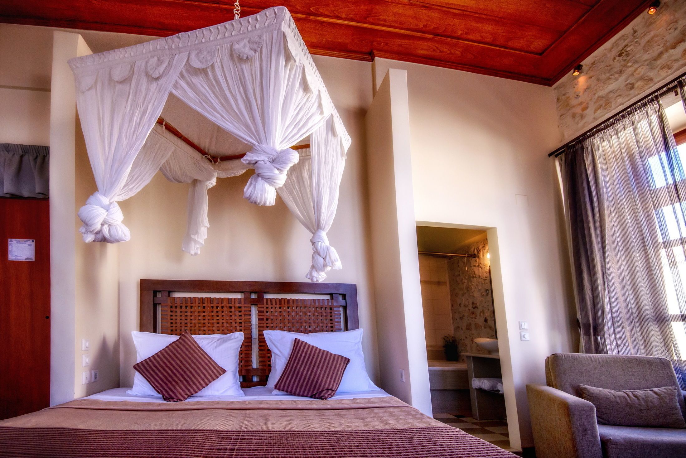 A bedroom with a canopy bed, wooden headboard, and a view of the bathroom.
