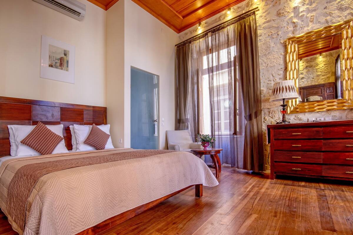 Un dormitorio con una cama grande, cabecera de madera, una silla, un aparador y un espejo con marco decorativo.