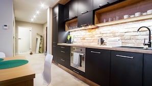A modern kitchen with black cabinets, a brick backsplash, and a wooden countertop. - Old Town Luxury Apartments by Amstra (Kraków)