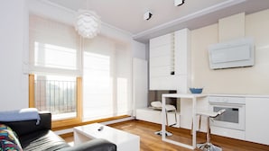 A modern living room with a black leather sofa, a white coffee table, and a large window with blinds. - Old Town Luxury Apartments by Amstra (Kraków)