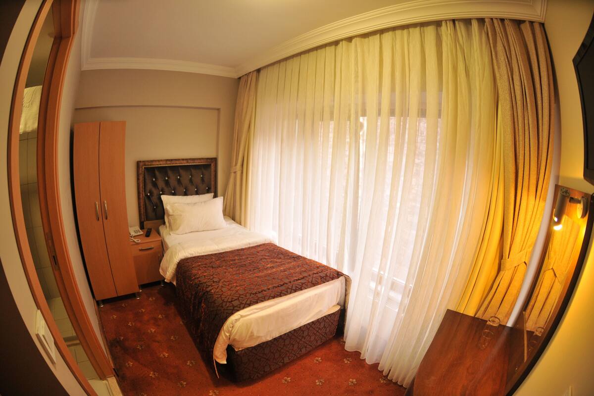 A hotel room with a bed, a wardrobe, a nightstand, and a large window with curtains.