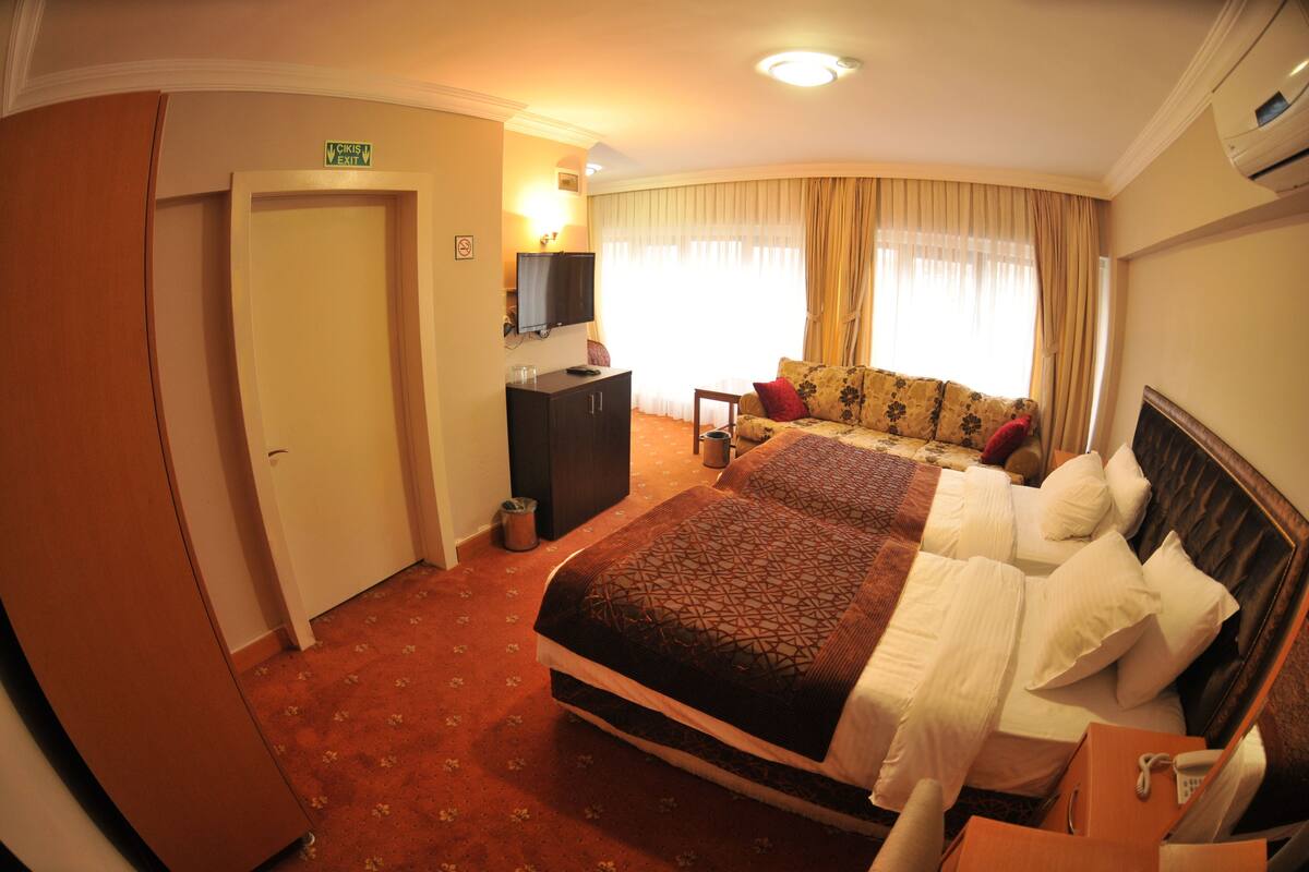 A hotel room with a large bed, a sofa, a TV, and a desk.