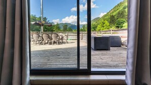 Vista desde el interior de una habitación con un amplio ventanal que da a una terraza exterior con sillas y una mesa.