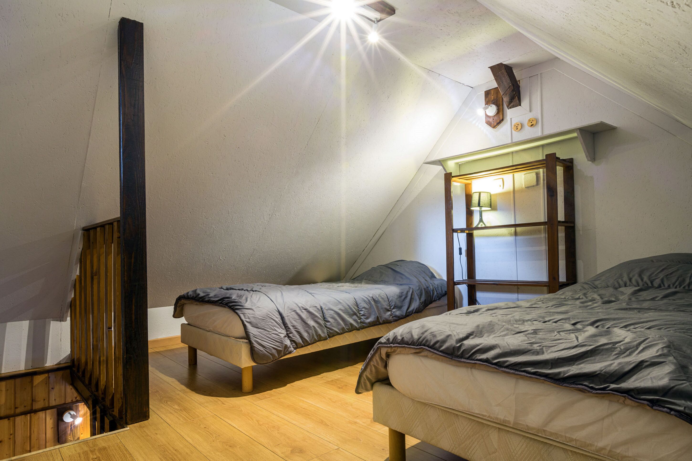 A small, cozy attic bedroom with two single beds, wooden flooring, and a sloped ceiling.