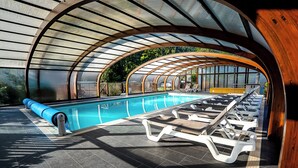 Una piscina interior moderna con techo curvo, sillones de descanso y vista despejada del entorno verde.