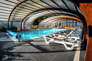 Una piscina interior moderna con techo curvo, sillones de descanso y vista despejada del entorno verde.