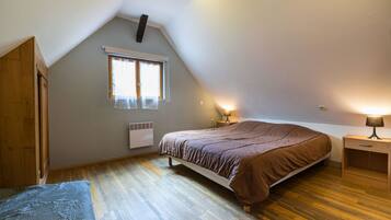 A bedroom with a sloped ceiling, a bed, a window with curtains, a bedside table with a lamp, and a radiator.