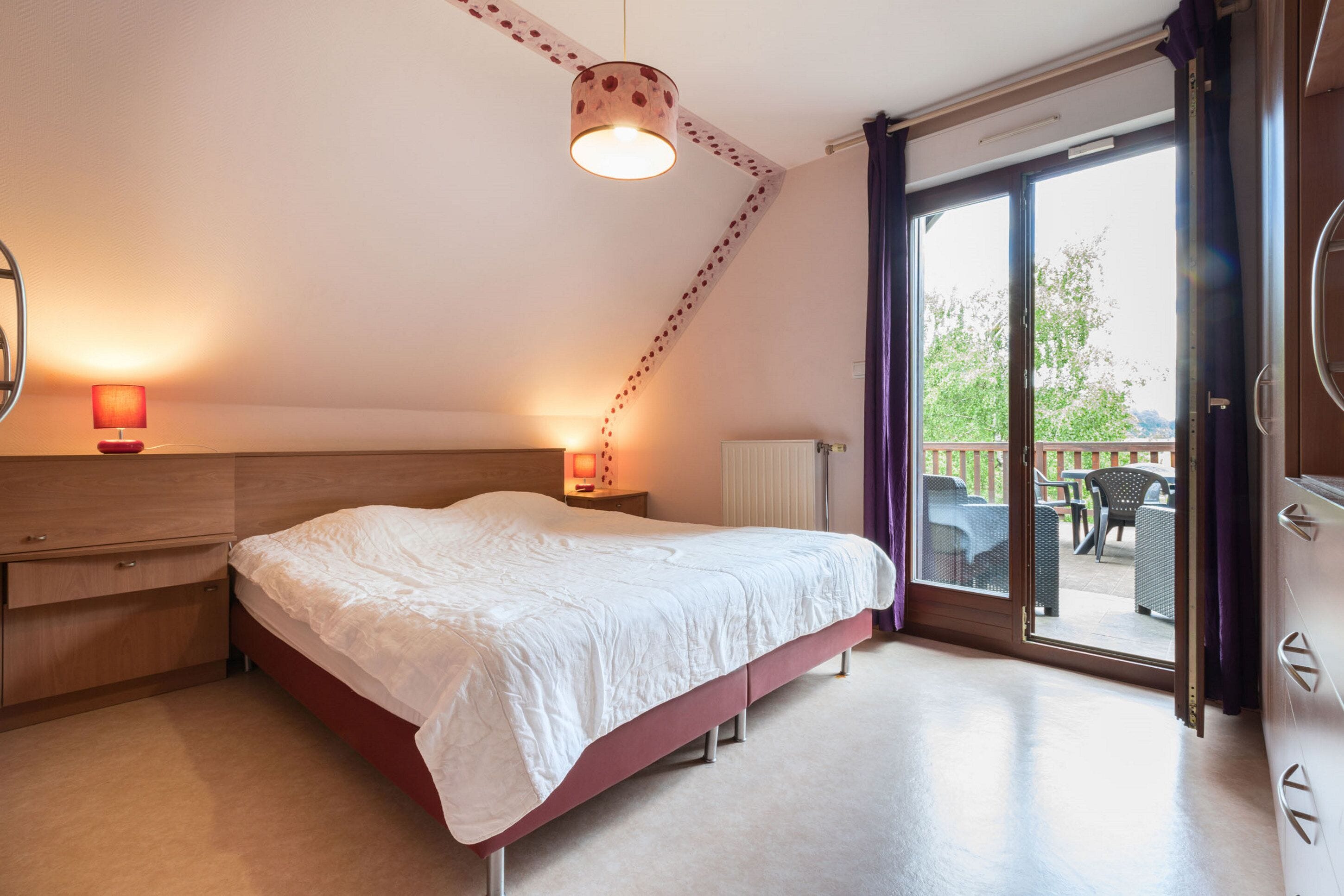 A bedroom with a bed, bedside lamps, a window, and a view of the outside.