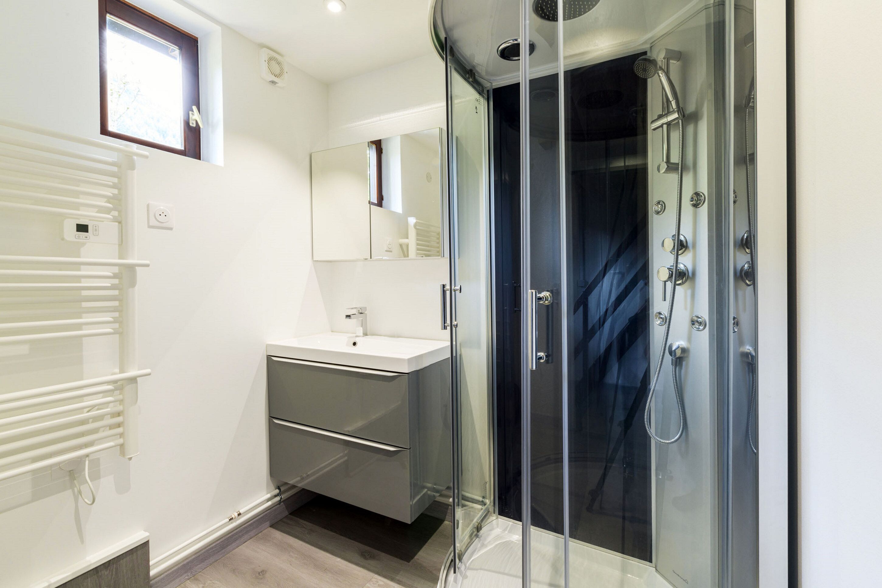 Un baño moderno con ducha envuelta en vidrio, un lavamanos blanco y un espejo sobre el mueble.