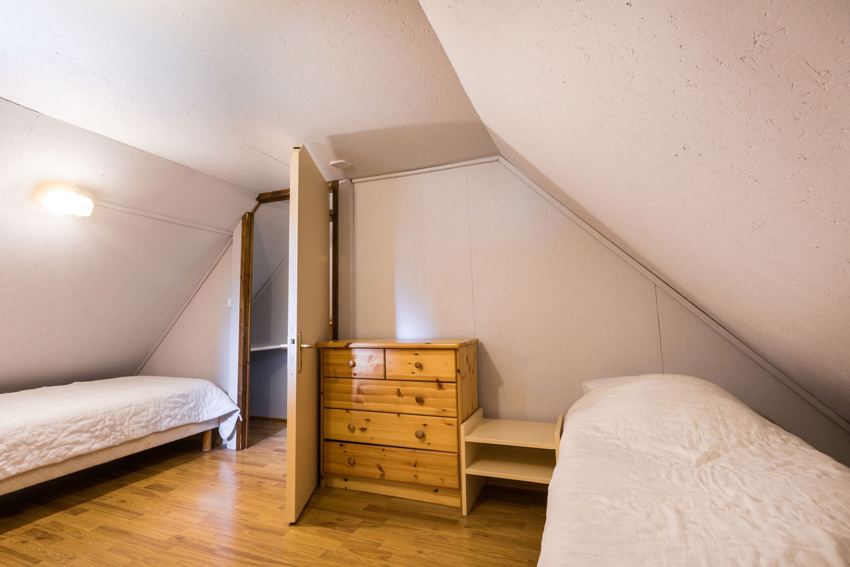 A small, triangular attic bedroom with two single beds, a wooden dresser, and a slanted ceiling.