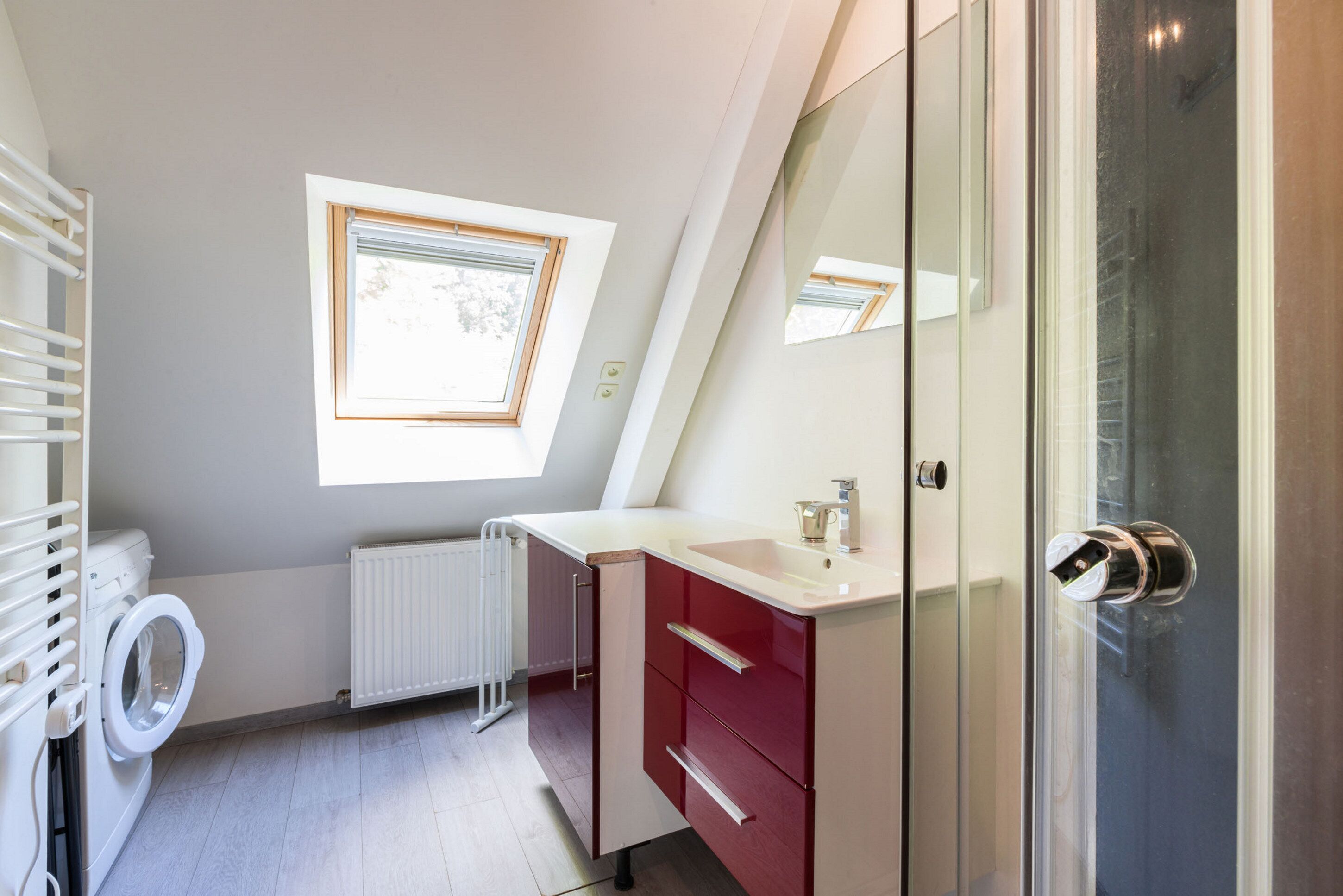Un baño moderno con lavadora integrada, cabina de ducha de vidrio y tragaluz.
