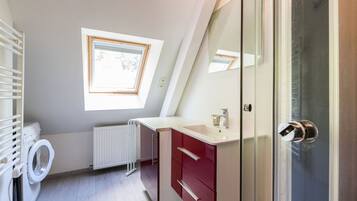 Un baño moderno con lavadora integrada, cabina de ducha de vidrio y tragaluz.