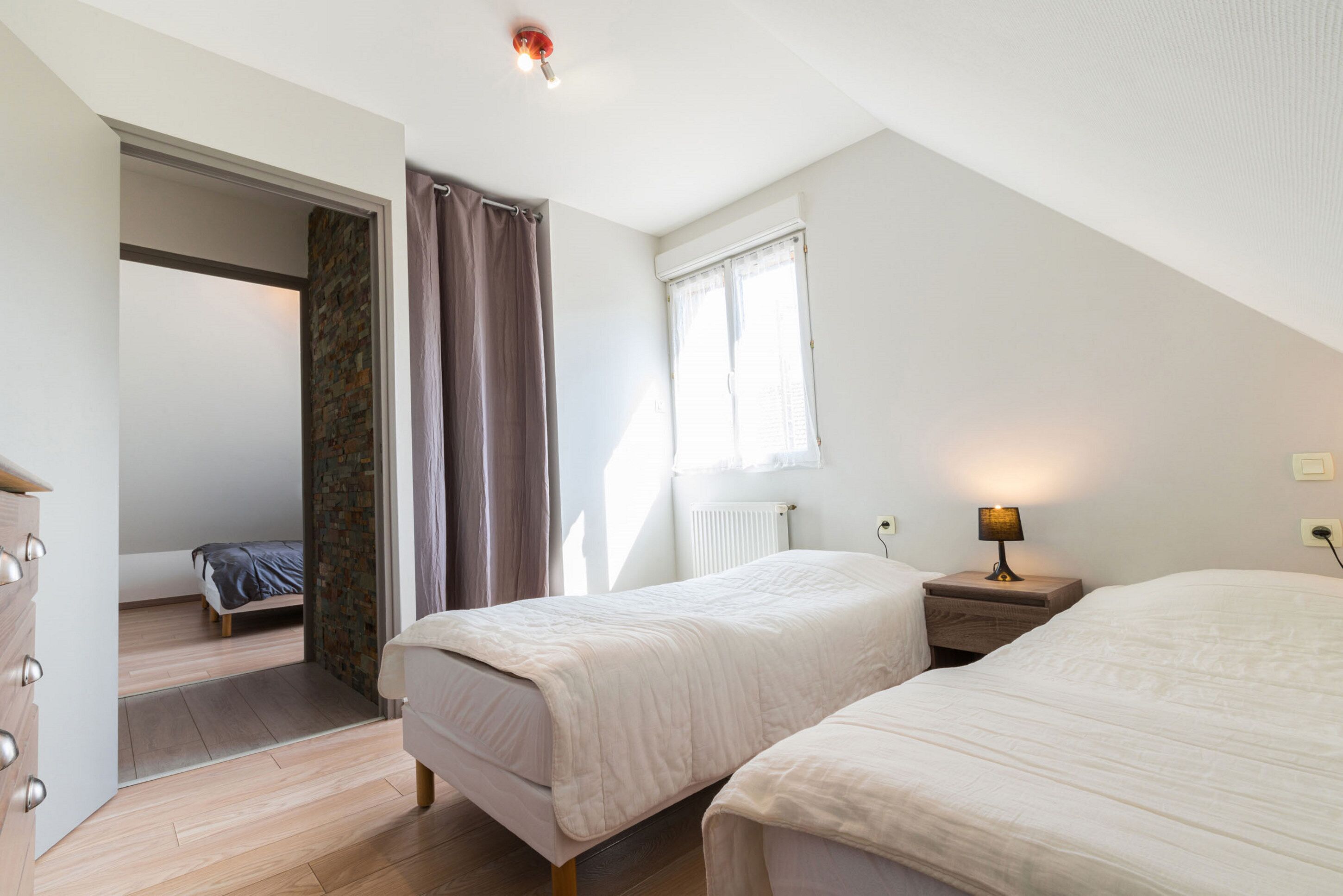 Un dormitorio con dos camas, un aparador de madera, un radiador y una ventana con cortinas.
