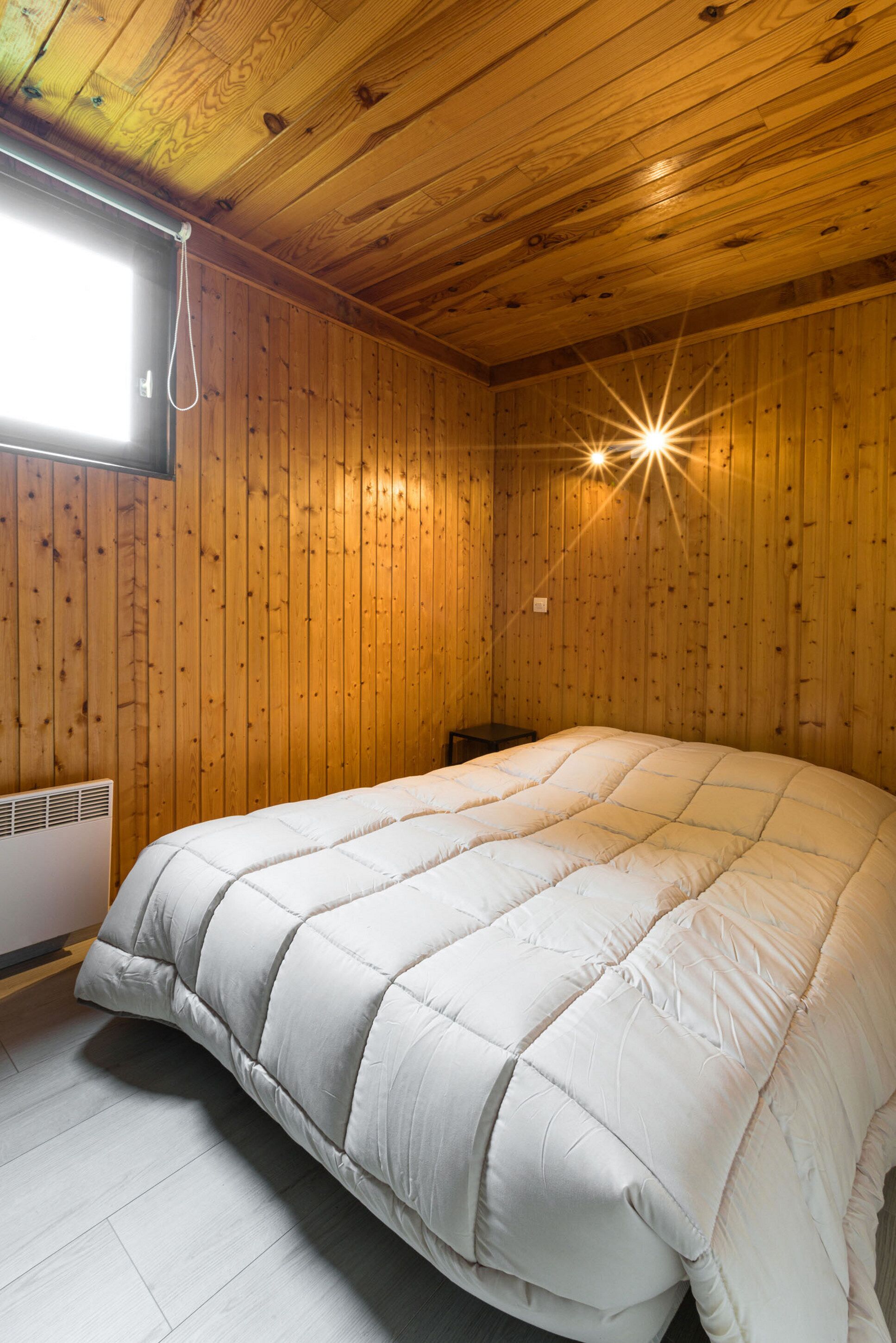 Une pièce aux murs en bois, avec un grand lit, un radiateur et une fenêtre.