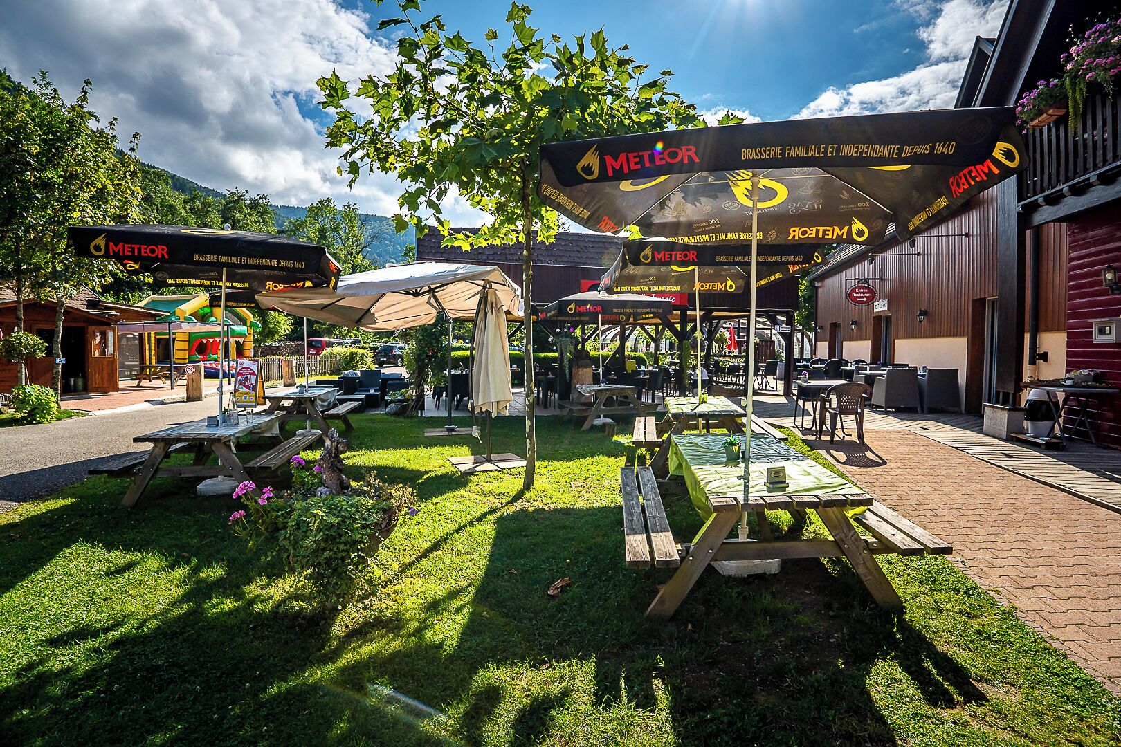 An outdoor dining area with tables and umbrellas branded with 'METEOR'.