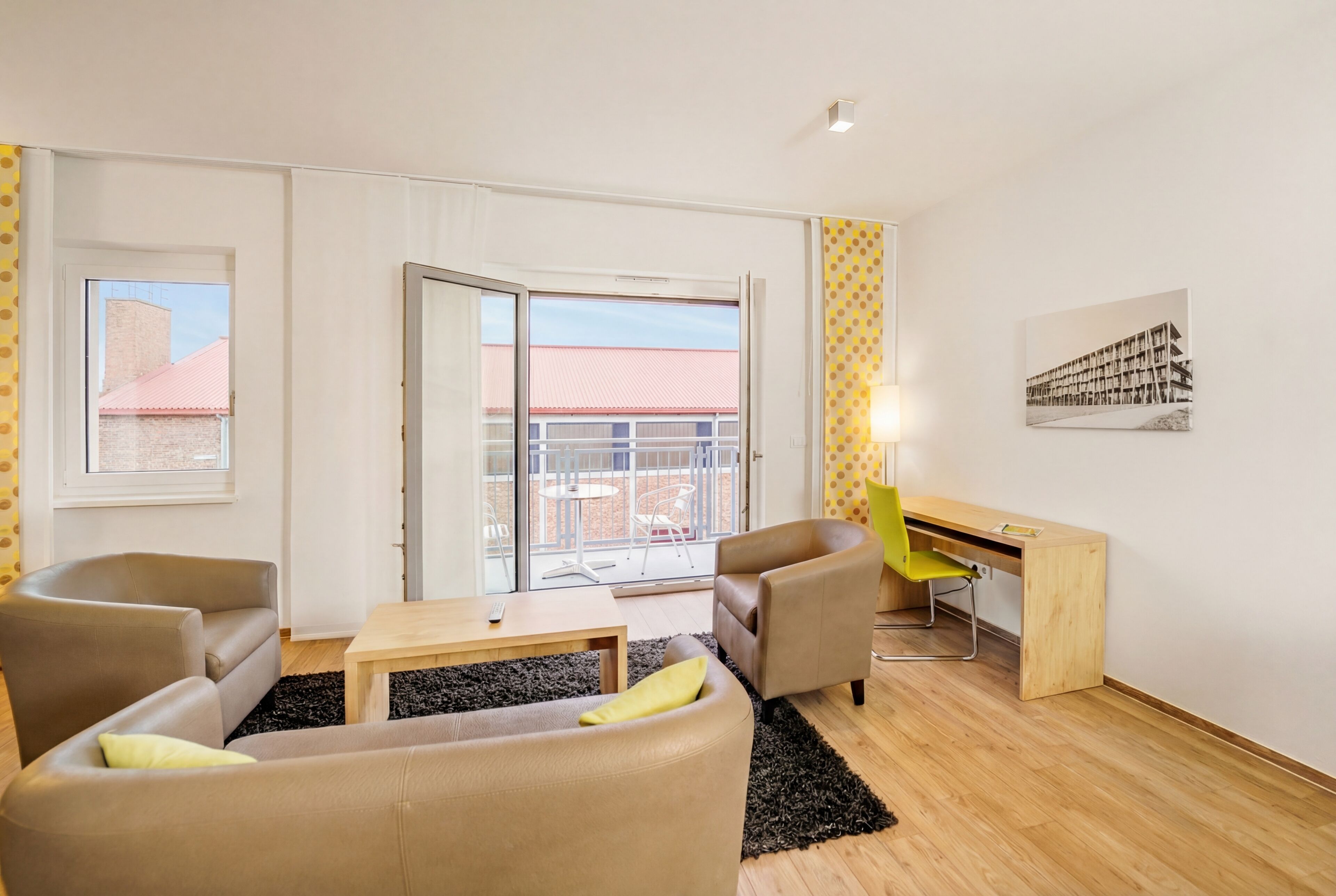 En moderne stue med sofa, stole, et skrivebord og en balkon med udsigt.