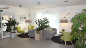 A modern lobby with a seating area, potted plants, and a large window with sheer curtains. - ADAPT APARTMENT HOTEL Berlin-Adlershof (Berlin)