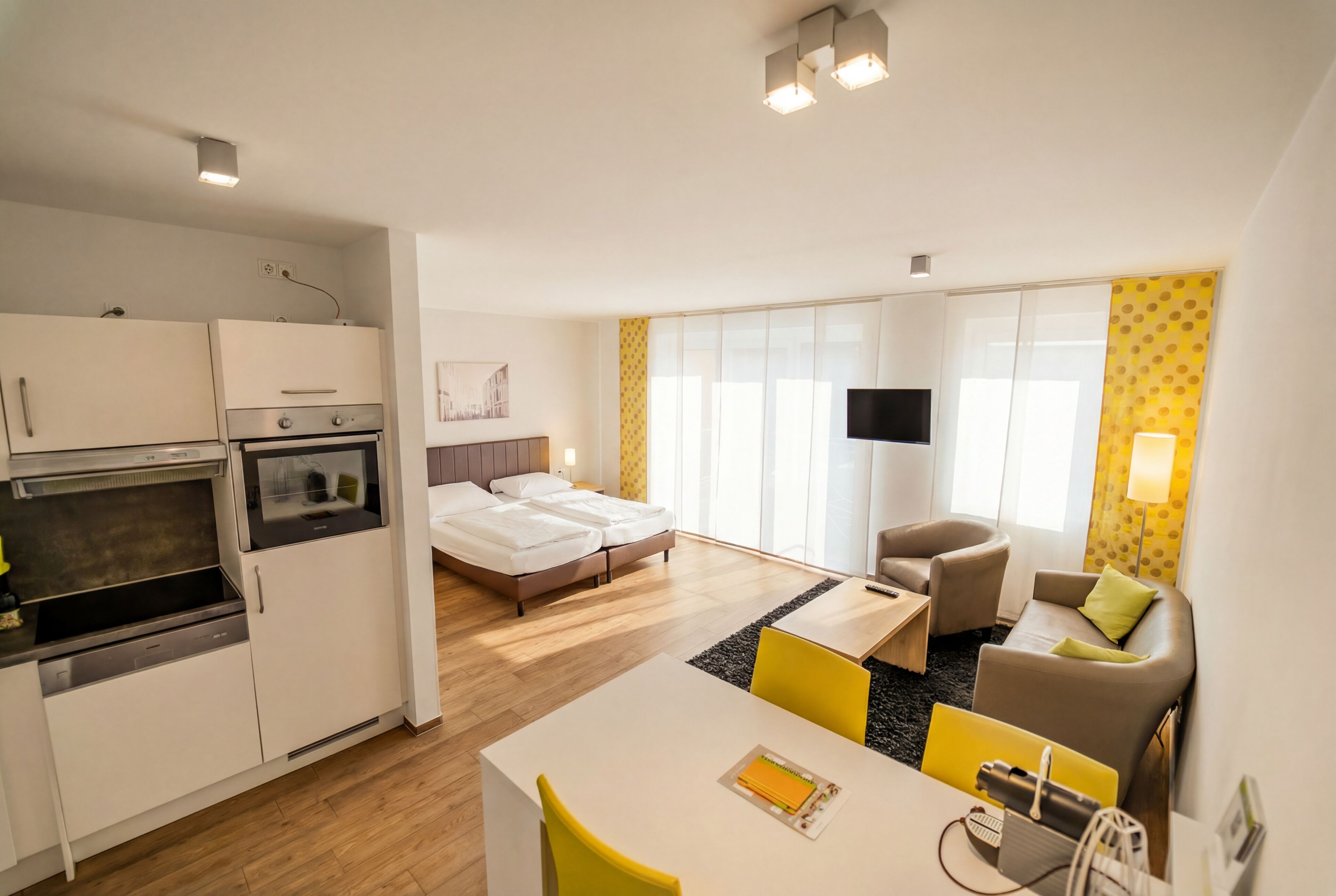 Una habitación de hotel moderna con kitchenette, una cama, un televisor y una zona de estar.