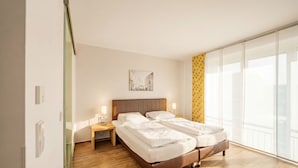 Une chambre d’hôtel moderne dotée d’un grand lit, d’une table de chevet, d’une petite table et d’une grande fenêtre offrant une vue agréable.
