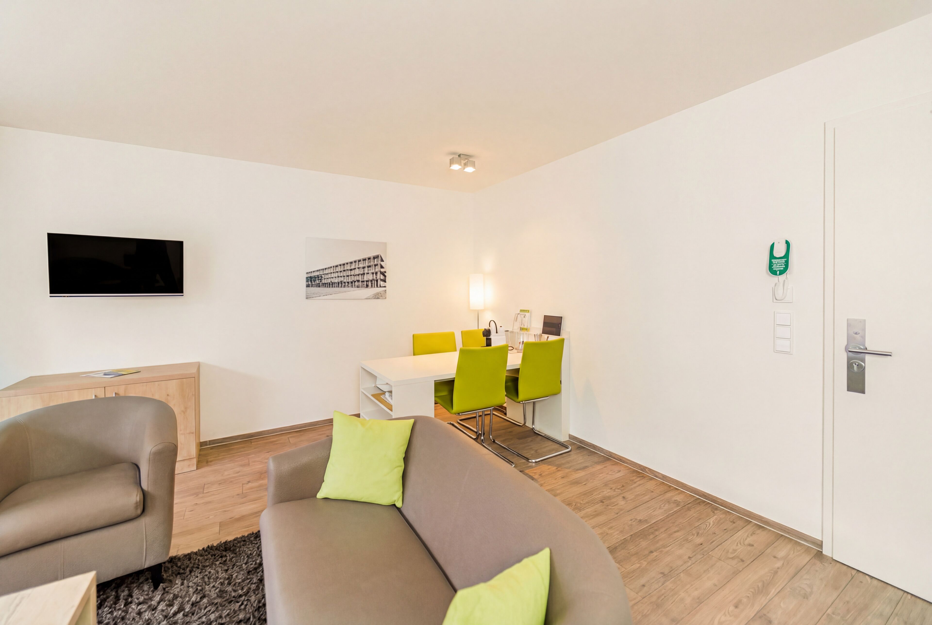 A modern living room with a sofa, a TV, a dining area with chairs, and a door with a lock.