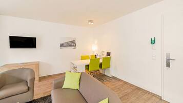 A modern living room with a sofa, a TV, a dining area with chairs, and a door with a lock.