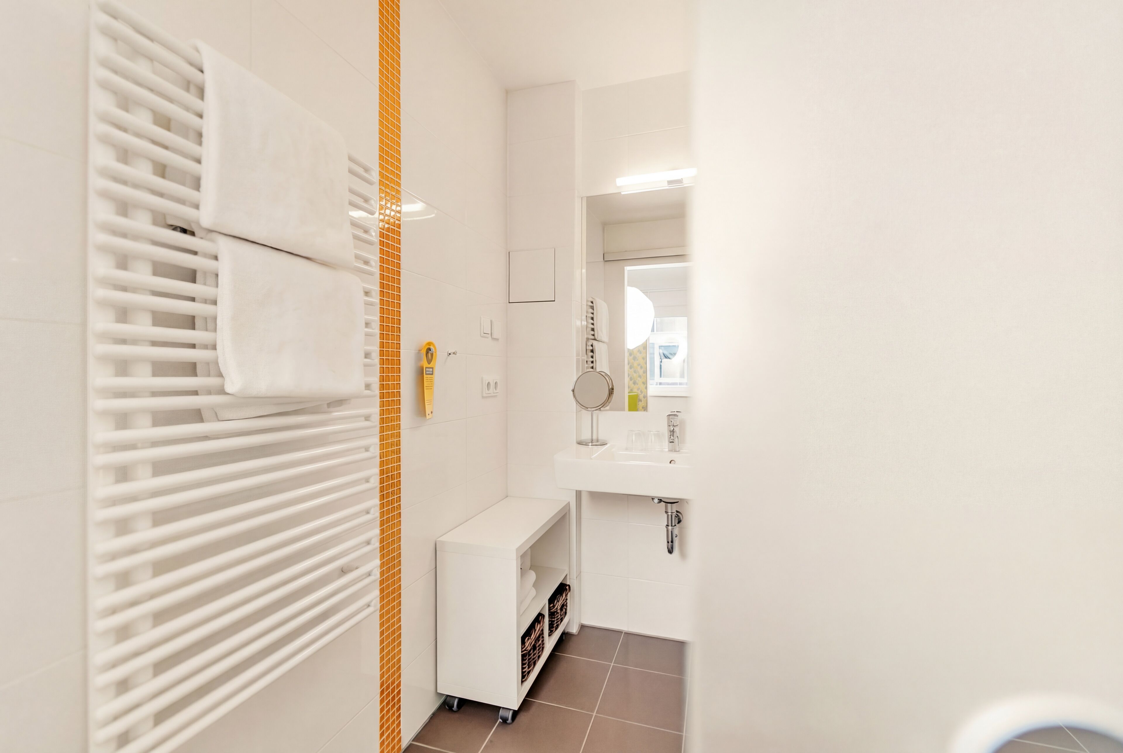 Un bagno con termosifone bianco, un piccolo mobiletto e uno specchio sopra il lavandino.