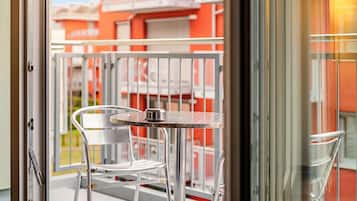 Un balcone con una sedia e un tavolo in metallo, una porta-finestra in vetro e vista su un edificio dai colori arancione e bianco.