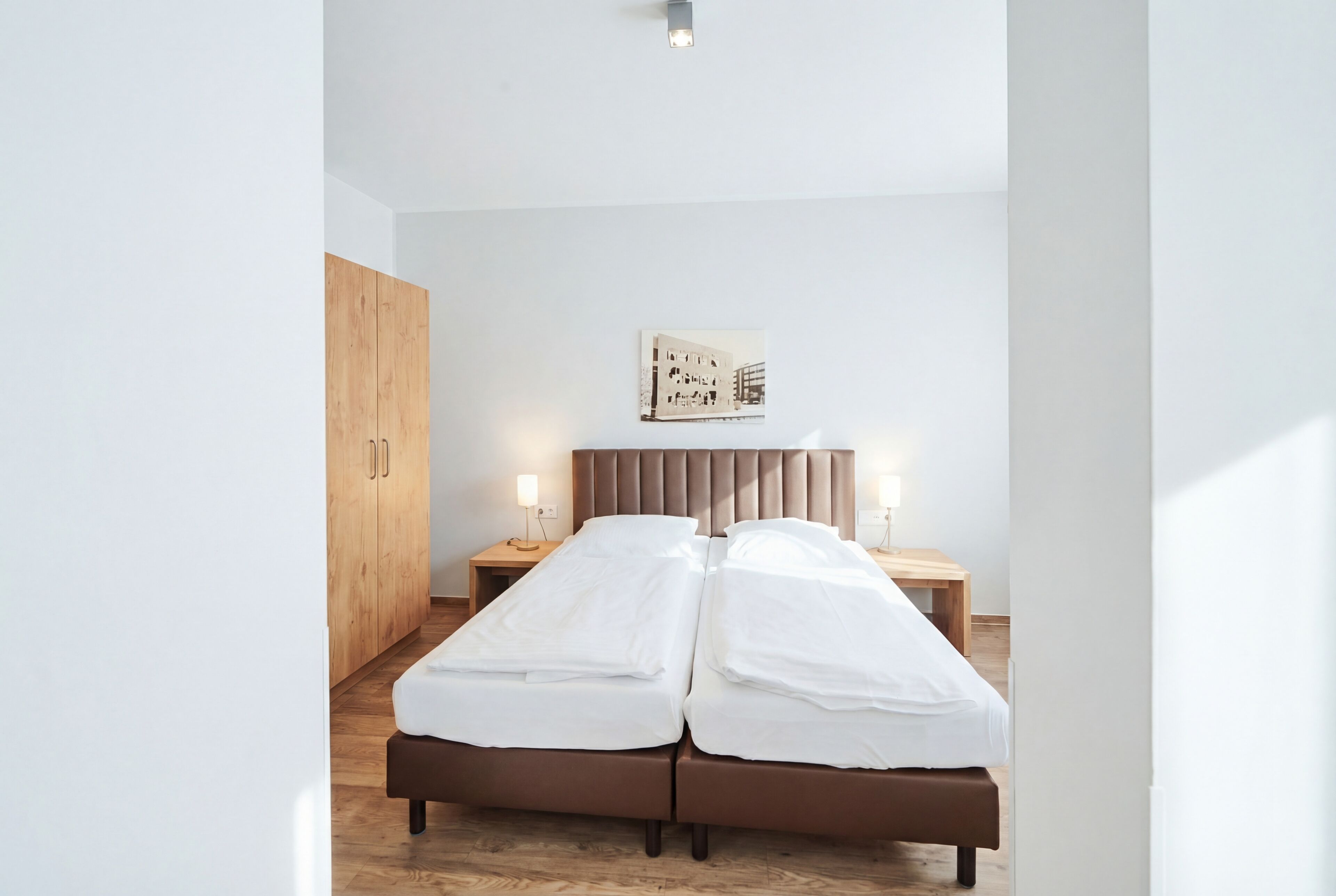 Una cama doble con cabecera de madera, dos mesitas de noche con lámparas, un armario de madera y un cuadro colgado en la pared.