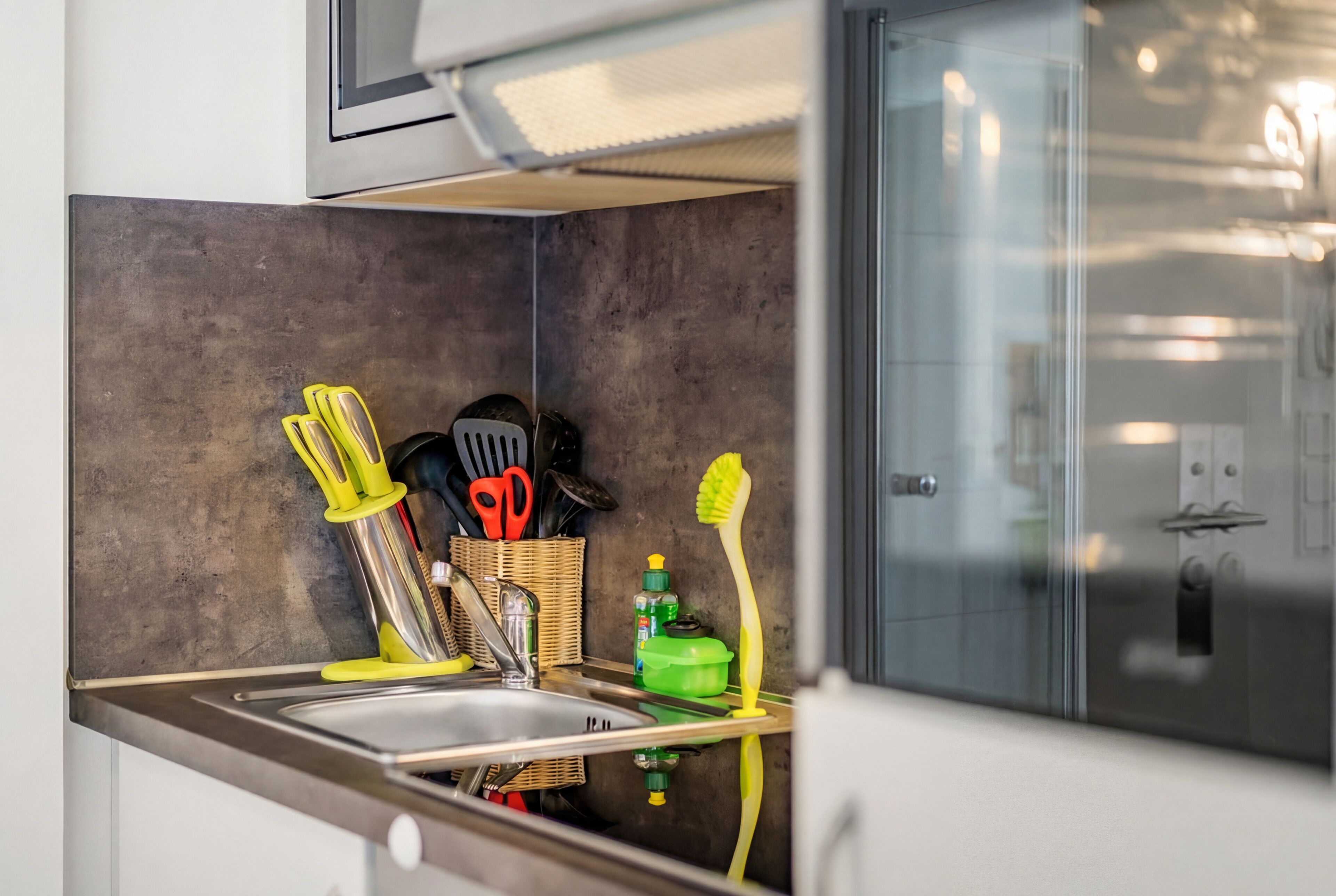 Cozinha com pia de aço inoxidável, micro-ondas e armário de vidro.
