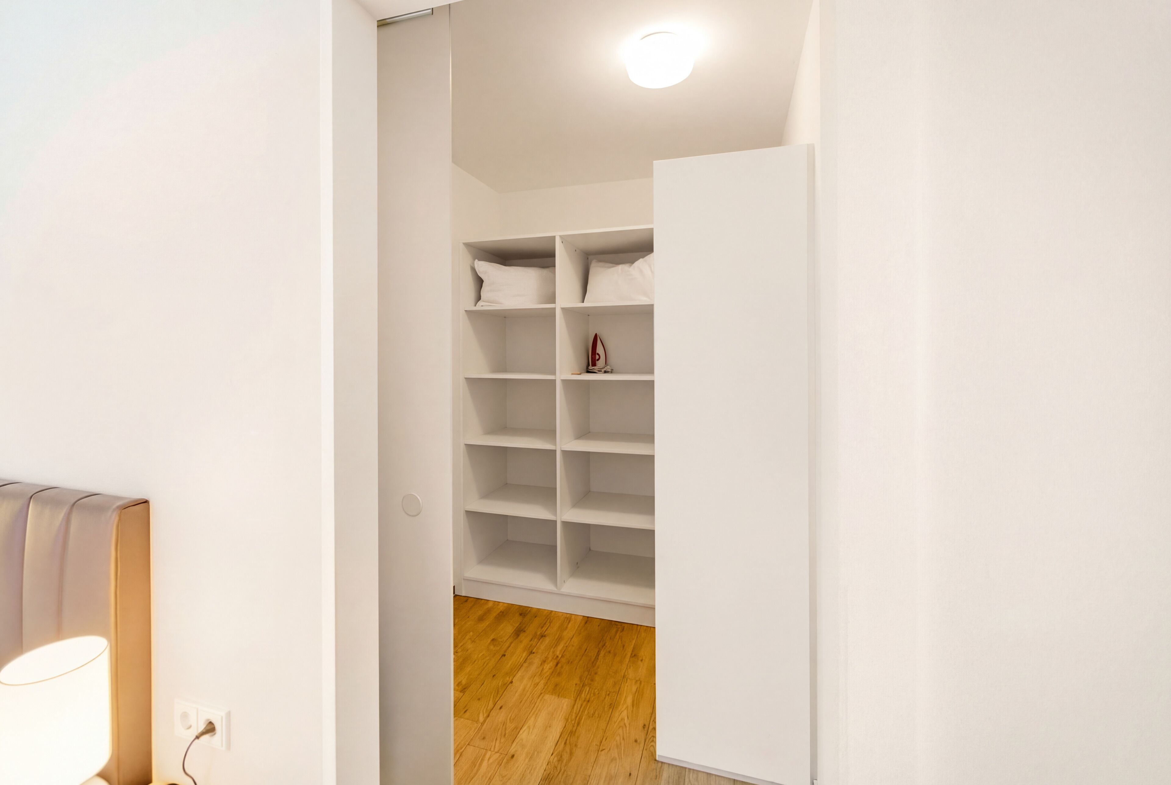 Un couloir étroit avec une armoire blanche et une lampe sur le côté gauche.