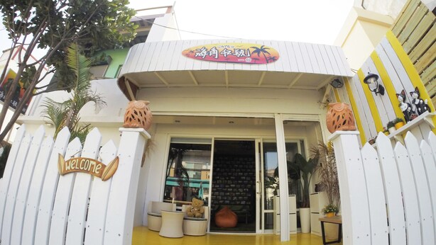 A building entrance with a 'Welcome' sign, a palm tree, and a yellow floor. - Cape 42 Hostel I (Hengchun)