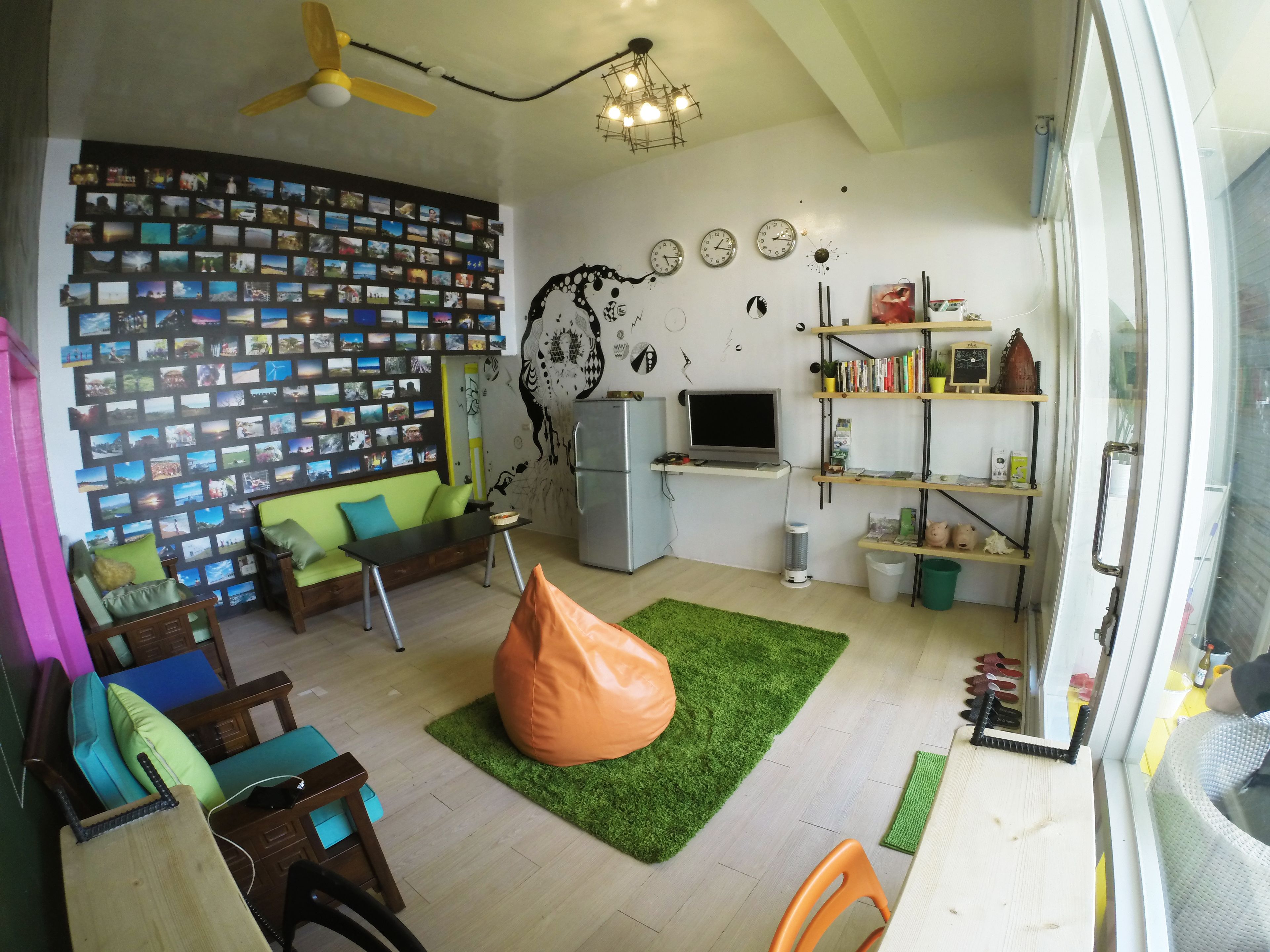 A living room with a sofa, chairs, a bean bag, a TV, a bookshelf, and a wall decorated with photos.