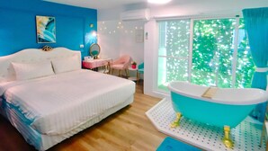 Un dormitorio con una cama grande, un tocador con espejo, una mesita y una ventana con vistas a la vegetación.