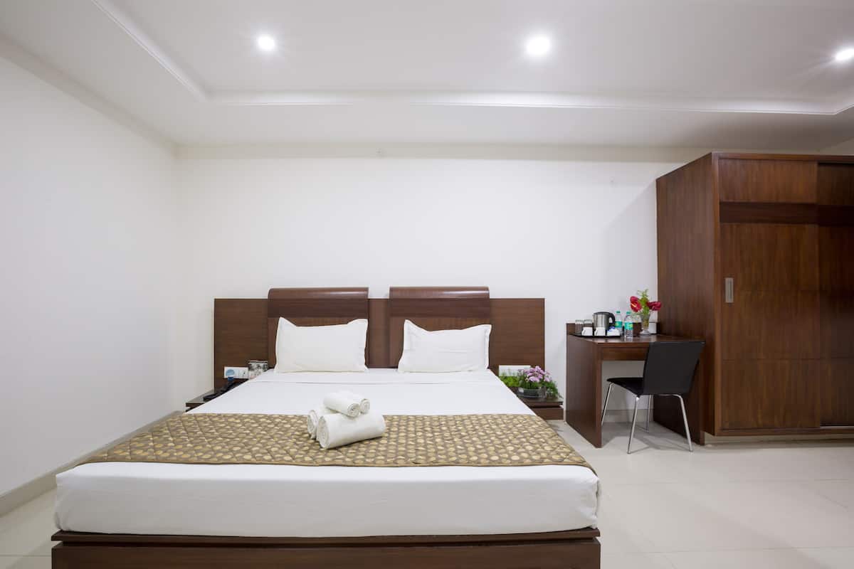 Ein Hotelzimmer mit einem großen Bett, einem Holzschrank, einem Schreibtisch mit Stuhl sowie einem kleinen Tisch mit Blumenvase.